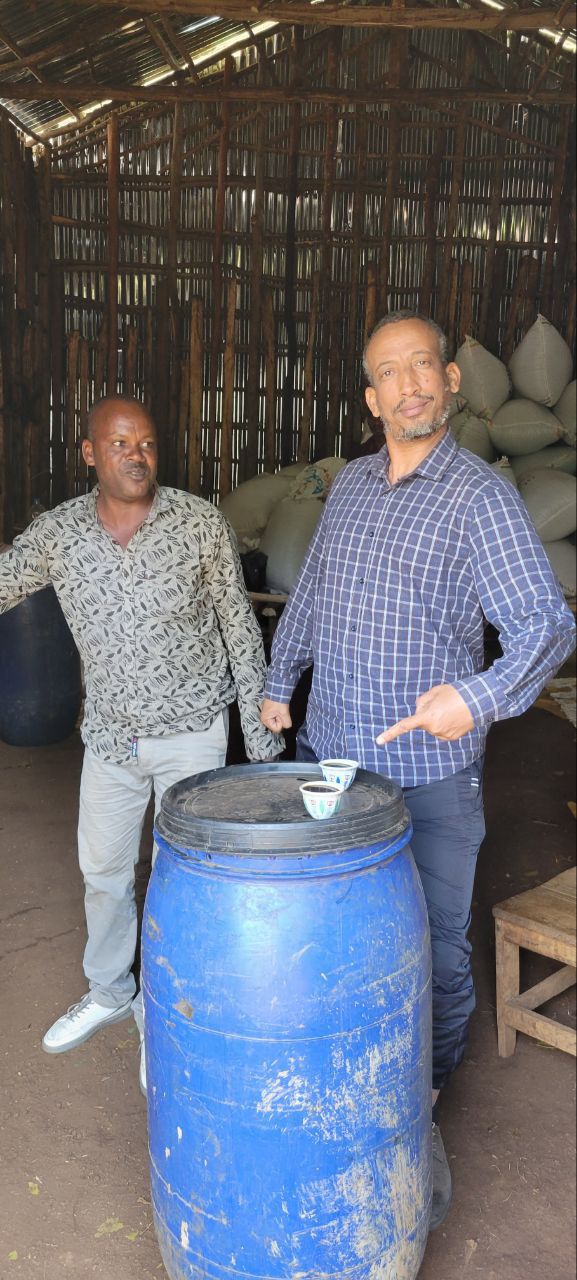 Bekele Yutute standing next to a blue barrel inside a rustic building with wooden walls.