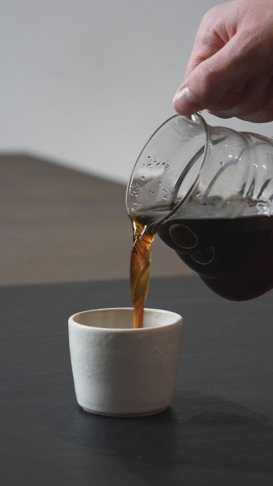 Person pouring coffee from a glass carafe into a white cup