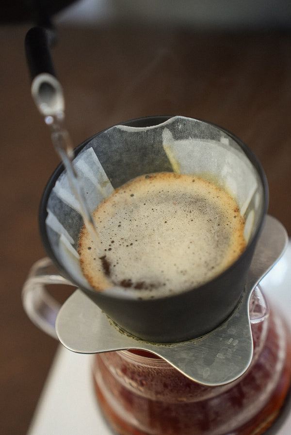 Coffee being brewed into a filter with steam rising, on a wooden surface.
