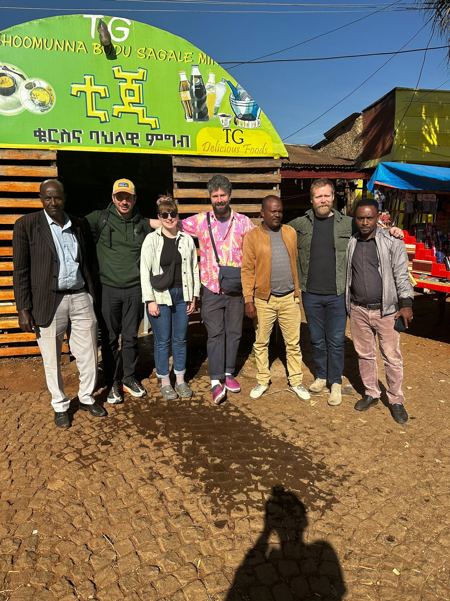 Group of people standing in front of a green building with signage.