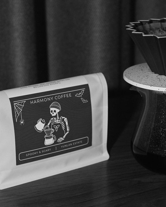 Close-up of the Spooky & Scary YunLan Estate bag label: a skeleton barista pouring filter coffee, with bats and a spider web