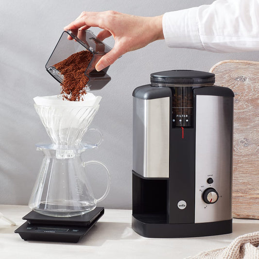 The best filter coffee grinders 2025, person pouring coffee grinds into a v60 from a Wilfa