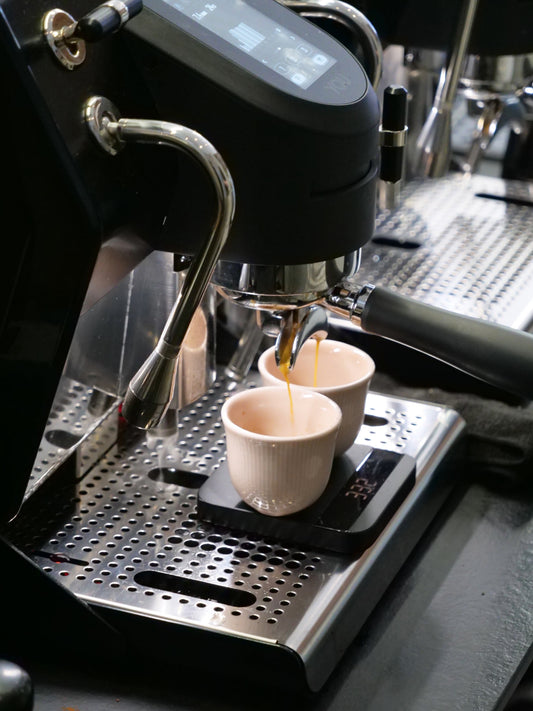 Cafe coffee calculator: A photo of two cups of espresso being brewed onto a set of scales on an espresso machine in a modern cafe setting.