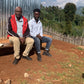 Two men sitting on a wooden bench outdoors with a scenic background