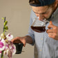 Man holding a glass carafe of coffee with a flower arrangement in the foreground