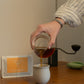 Consuelo Rubio Anaerobic sidra coffee poured into a cup on a table from a glass carafe, with a commandant c40 in the background