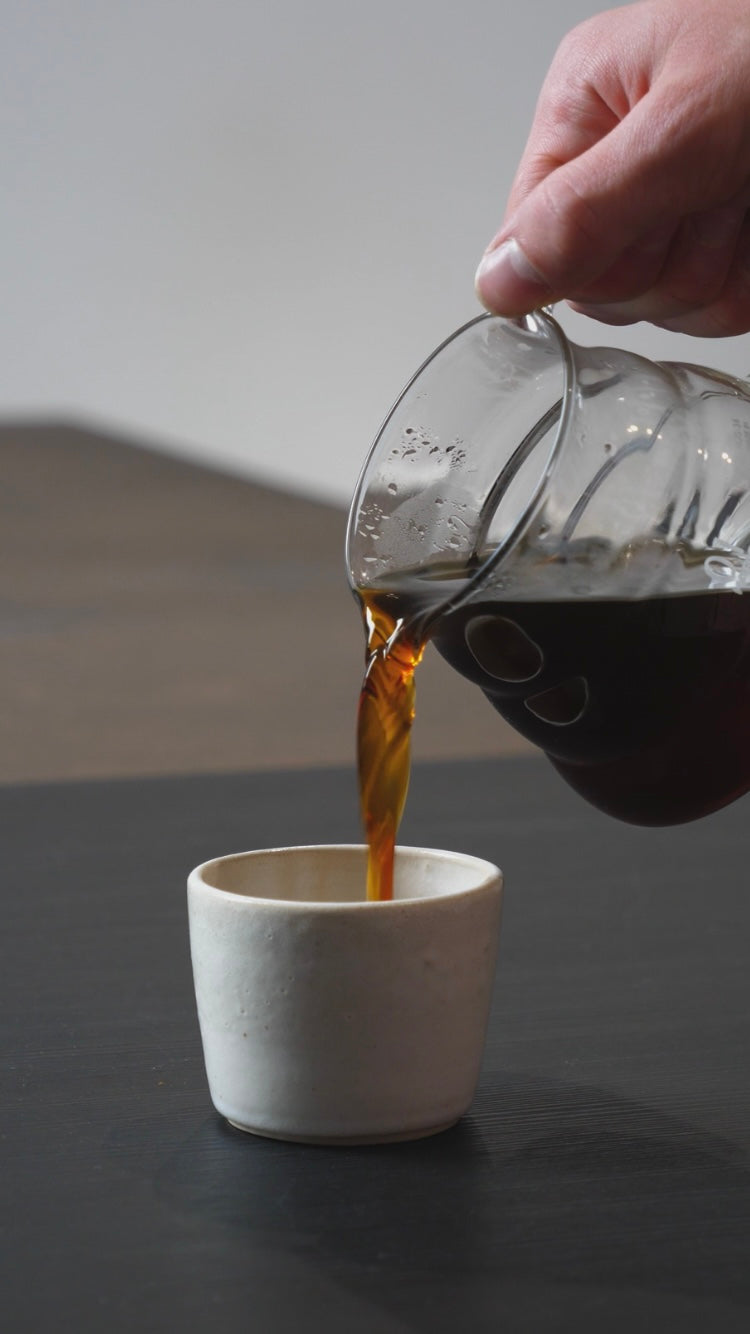Person pouring coffee from a glass carafe into a white cup 