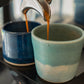 Espresso being poured into a blue ceramic cup from an espresso machine.