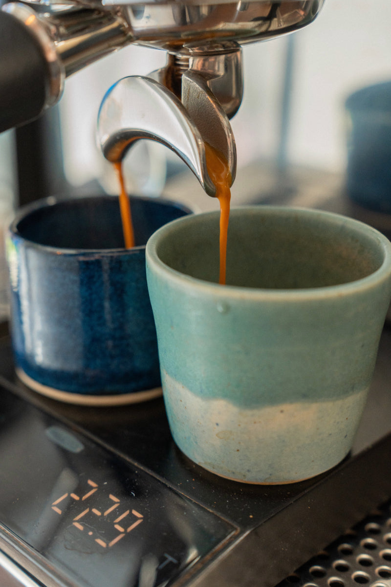 Espresso being poured into a blue ceramic cup from an espresso machine.