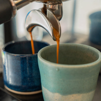 Espresso being poured into two ceramic cups from an espresso machine.
