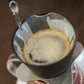 Coffee being brewed into a filter with steam rising, on a wooden surface.