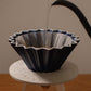 Black ceramic coffee filter being filled with water on a white stand against a neutral background