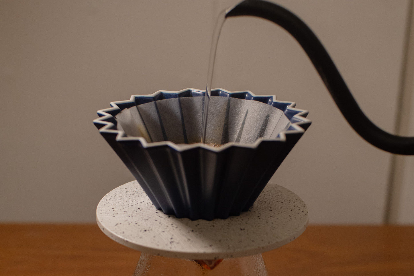 Black ceramic coffee filter being filled with water on a white stand against a neutral background