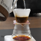 Brewista coffee maker pouring water into a glass carafe on a dark surface.