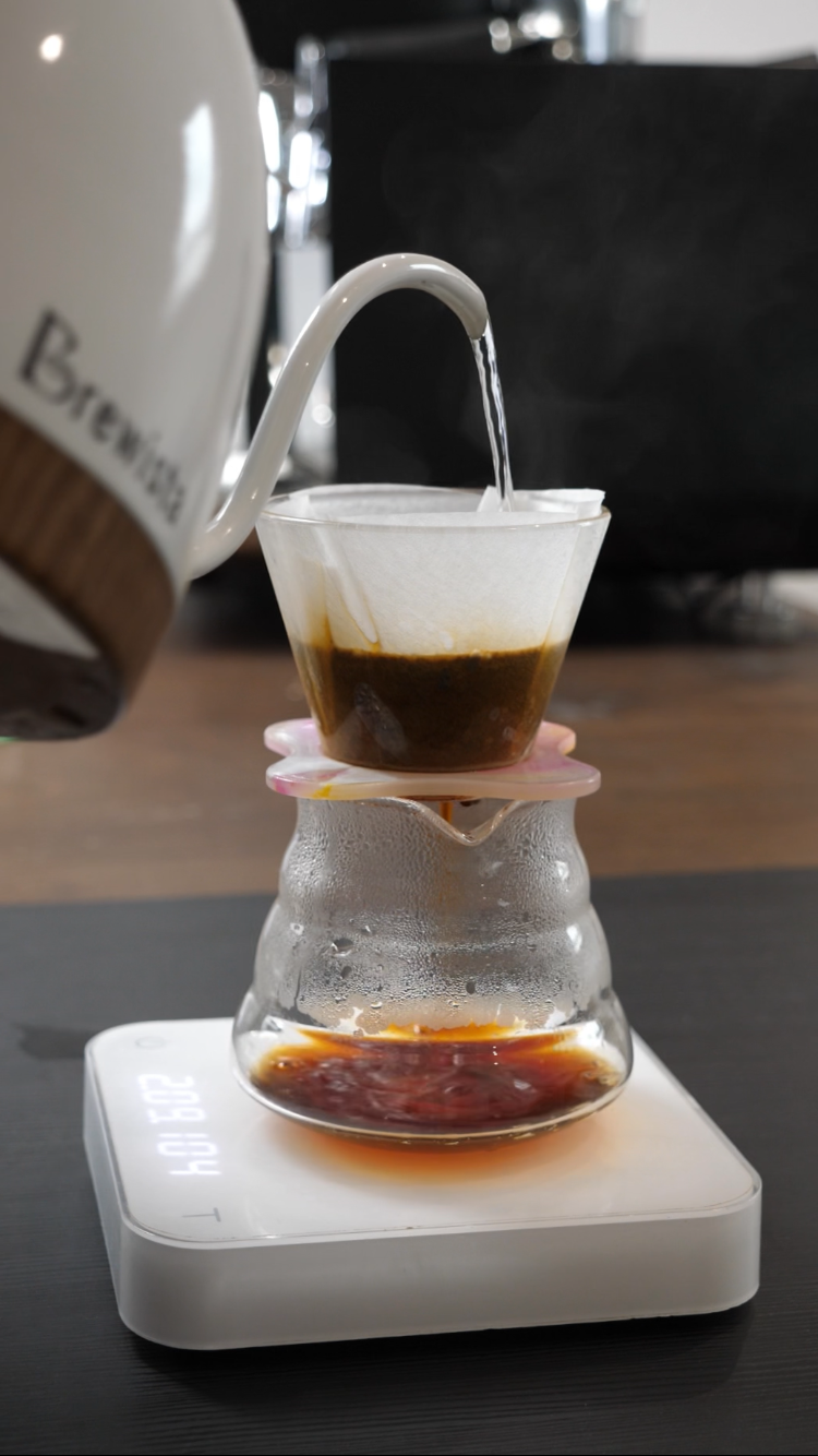 Brewista coffee maker pouring water into a glass carafe on a dark surface.