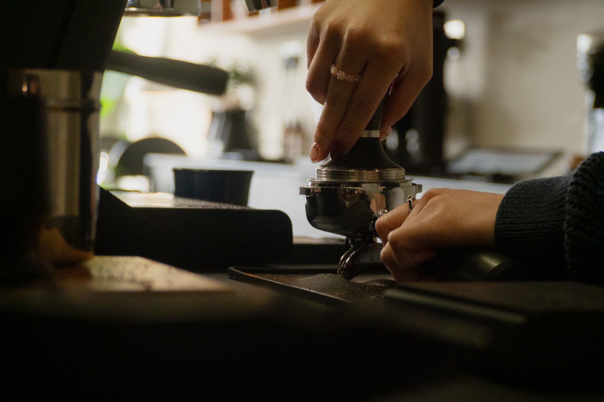Person using a coffee tamper to manually tamp a bed of coffee in a cafe setting